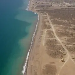 Vista aérea de la playa Torregarcia, con el mar turquesa a la izquierda y la costa arenosa con vegetación escasa y construcciones a la derecha.