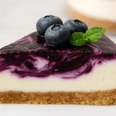 Rebanada de pastel de arandanos con cobertura de arándanos y tres bayas frescas encima.
