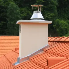 Nowy, metalowy nasadnik kominowy na dachu z pomarańczowej dachówki. Rozwiązanie to może pomóc jak poprawić ciąg w kominie.