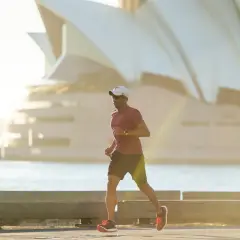 Mężczyzna w czapce i okularach biega przy wodzie, budując bazę tlenową. W tle widać charakterystyczne żagle Opery w Sydney.