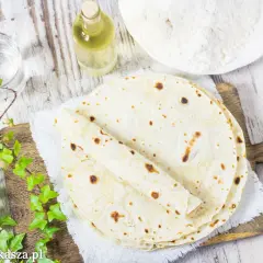 Stos świeżo upieczonych tortilli na desce, obok mąka, woda i olej.