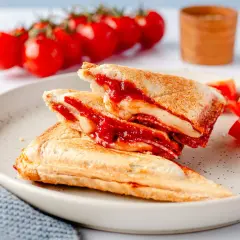 Herzhafte Sandwichmaker Rezepte: goldbraune Sandwiches mit geschmolzenem Käse und Tomatensoße, serviert mit frischen Tomaten.