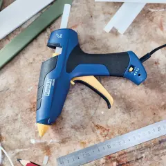 Pistolet à colle bleu et jaune, prêt à l'emploi pour apprendre comment coller du plastique. Des bâtons de colle et des règles sont à proximité.