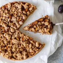 Ein köstlicher, gesunder Pflaumenkuchen mit knuspriger Streuseldecke. Ein Stück wird gerade herausgehoben.