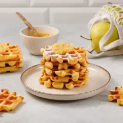 Goldbraune Waffeln mit Apfelmus bestreut, daneben eine Schüssel mit Apfelmus und ein grüner Apfel im Netzbeutel.