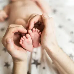 Dłonie otaczają maleńkie stópki 7 tygodniowego dziecka. Delikatne paluszki i pięty są objęte czułością.