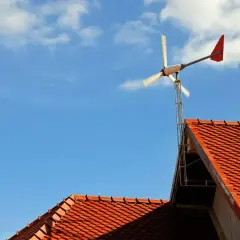 Wiatraki przydomowe na tle błękitnego nieba z chmurami, zamontowane na dachu z czerwonej dachówki.