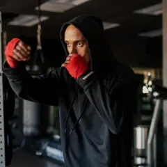 A man in a black hoodie with red hand wraps practices shadow boxing, his intense gaze reflecting the mental discipline of the sport.