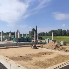 Budowa domu w toku. Widać fundamenty, betonowe słupy i hałdy piasku, który czeka na zagęszczenie.