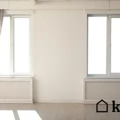 Nowoczesna osłona na stary kaloryfer pod oknem, z szarymi zasłonami po bokach.