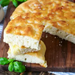 Frisch gebackene Focaccia, ein köstliches original focaccia rezept, mit Tomaten, Oliven und Basilikum auf einem Holzbrett.