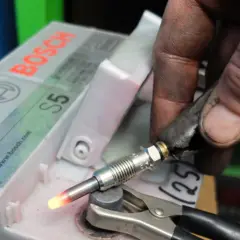 Ręka mechanika testuje rozgrzany przekaznik świec żarowych podłączony do akumulatora Bosch S5.