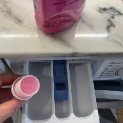 Hand hält Dosierkappe mit rosa Flüssigkeit. Waschpulver direkt in die Trommel geben? Nein, hier in die Schublade.