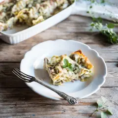 Una fetta di lasagne con carciofi surgelati, guarnita con menta, su un piatto bianco, accanto a una forchetta.
