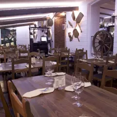 Mysig restaurangmiljö med träbord och stolar, dukade för middag. En rustik känsla med gamla redskap på väggen, som en inbjudande la terazza.