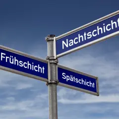 Wegweiser mit "Frühschicht", "Nachtschicht" und "Spätschicht". Hier gibt es Tipps zur Befreiung von Schichtarbeit.