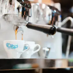 Gorąca kawa spływa do filiżanki z logo "Celberg Coffee". Zaparzacz paruje, sugerując idealne cappuccino ile ml.