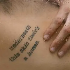 Mądre cytaty na tatuaż po angielsku: "Underneath this skin there's a human". Dłoń na mokrej skórze.