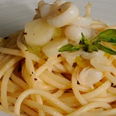 Deliciosos espaguetis con calamares, un plato de pasta con trozos de calamar y hojas verdes, servido en un cuenco blanco.