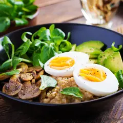 Pyszny bowl sniadaniowy z jajkiem na twardo, awokado, pieczarkami i świeżą sałatką na drewnianym stole.