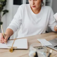 Mujer revisa facturas y escribe en agenda. El heredero no paga gastos vivienda, pero ella organiza las finanzas.