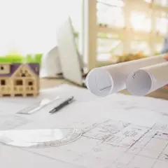 Plany budowy domu, makieta, rolki z projektami i przybory kreślarskie. Czas na rozpoczęcie budowy od uzyskania pozwolenia jest kluczowy.