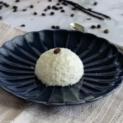 Semifreddo tartufo bianco, un dolce raffinato ricoperto di cocco e decorato con un chicco di caffè, su un piatto blu scuro.