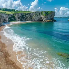 Plage de galets et falaises verdoyantes sous un ciel bleu avec des nuages blancs. Mer turquoise.