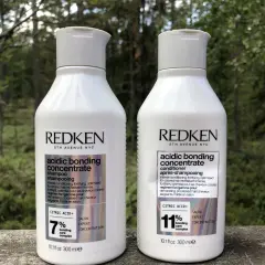 Två flaskor Redken Acidic Bonding Concentrate, schampo och balsam, står utomhus. Perfekt för att reparera skadat hår efter färgning.