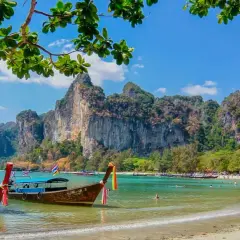 Två longtailbåtar guppar i det turkosa vattnet vid en vacker thailand strand. Imponerande klippor reser sig bakom den gröna djungeln.