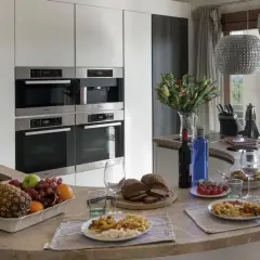 Cocina moderna con encimera curva, electrodomésticos integrados y vista al paisaje. Ideal para un contrato de alquiler temporal, con comida servida y frutas frescas.