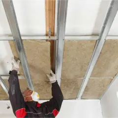 Man med mask och handskar monterar isolering i ett undertak. Bra för att isolera innertak och spara energi.
