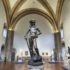 Donatello's David, a bronze masterpiece, stands triumphantly in a grand hall, surrounded by other sculptures and art.