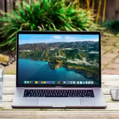 MacBook Pro z widokiem na wybrzeże Kalifornii. Obok szklanka wody, notatnik i telefon. Wiele marek laptopów oferuje podobne możliwości.