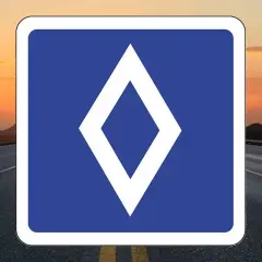 Un nouveau panneau routier bleu avec un losange blanc au centre, sur fond de route et de coucher de soleil.