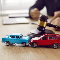 Modellini di auto blu e rossa che simulano un **infortunio in itinere** di circa 30 minuti, con un martelletto da giudice sullo sfondo.