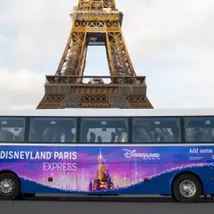 Un bus Disneyland Paris Express, décoré d'un château féerique, passe devant la Tour Eiffel.