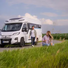 Para podróżuje kamperem Hobby, mając przy sobie carnet de passage. Cieszą się wolnością na tle pól kukurydzy.