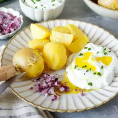 Kartoffeln mit Quark, garniert mit Schnittlauch und verfeinert mit Öl. Dazu gibt es gehackte rote Zwiebeln und ein Messer zum Schälen.