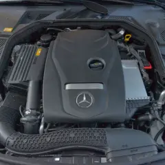 Silnik w mercedes benz klasa c. Widoczny jest czarny plastikowy wlot powietrza, zbiornik płynu chłodniczego i osłona silnika z logo producenta.