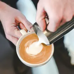 Barista versa latte art, mostrando come fare la schiuma al latte per un cappuccino perfetto.