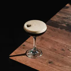 Elegancki Espresso Martini z pianką i ziarnem kawy na drewnianym stole. Idealny przepis na ten klasyczny drink.