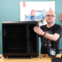 Mężczyzna pokazuje obudowę komputera, obok leży zasilacz i elementy do złożenia PC. Poradnik: jak złożyć komputer.