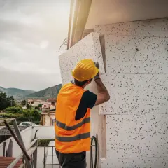 Operaio con casco giallo applica pannelli isolanti per il mini cappotto esterno di un edificio.