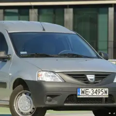 Srebrny Dacia Logan Van z polskimi tablicami WE 3495W zaparkowany przed nowoczesnym budynkiem.