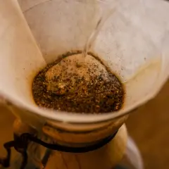 Woda powoli przelewa się przez zmieloną kawę w papierowym filtrze, tworząc aromatyczny napar w chemexie.