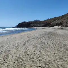 Arena dorada y mar azul en la almerimar playa, con montañas rocosas al fondo bajo un cielo despejado.