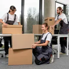 Tre persone in tuta grigia impacchettano scatole per svuotare casa.