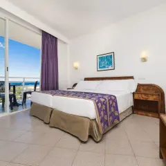 Pokój w hotelu Globales Palmanova Palace z widokiem na morze. Dwa łóżka, fioletowe zasłony i balkon.