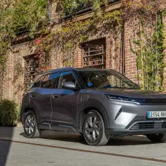 Un coche gris moderno, con matrícula 2154 NHG, aparcado frente a una pared de ladrillos cubierta de hiedra. Es el **atto 2** de la marca.